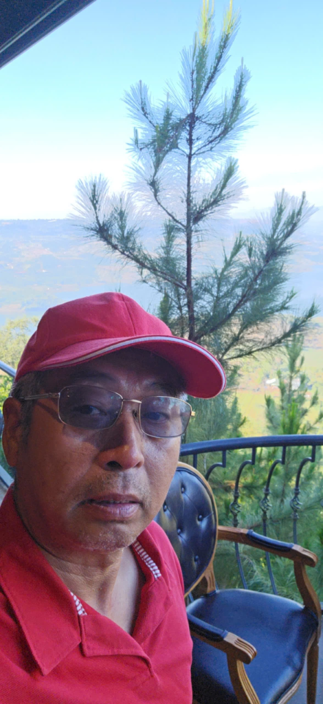 Anh Tuấn Hương - chân dung với mũ đỏ và kính, nhìn ra cao nguyên Di Linh từ ban công